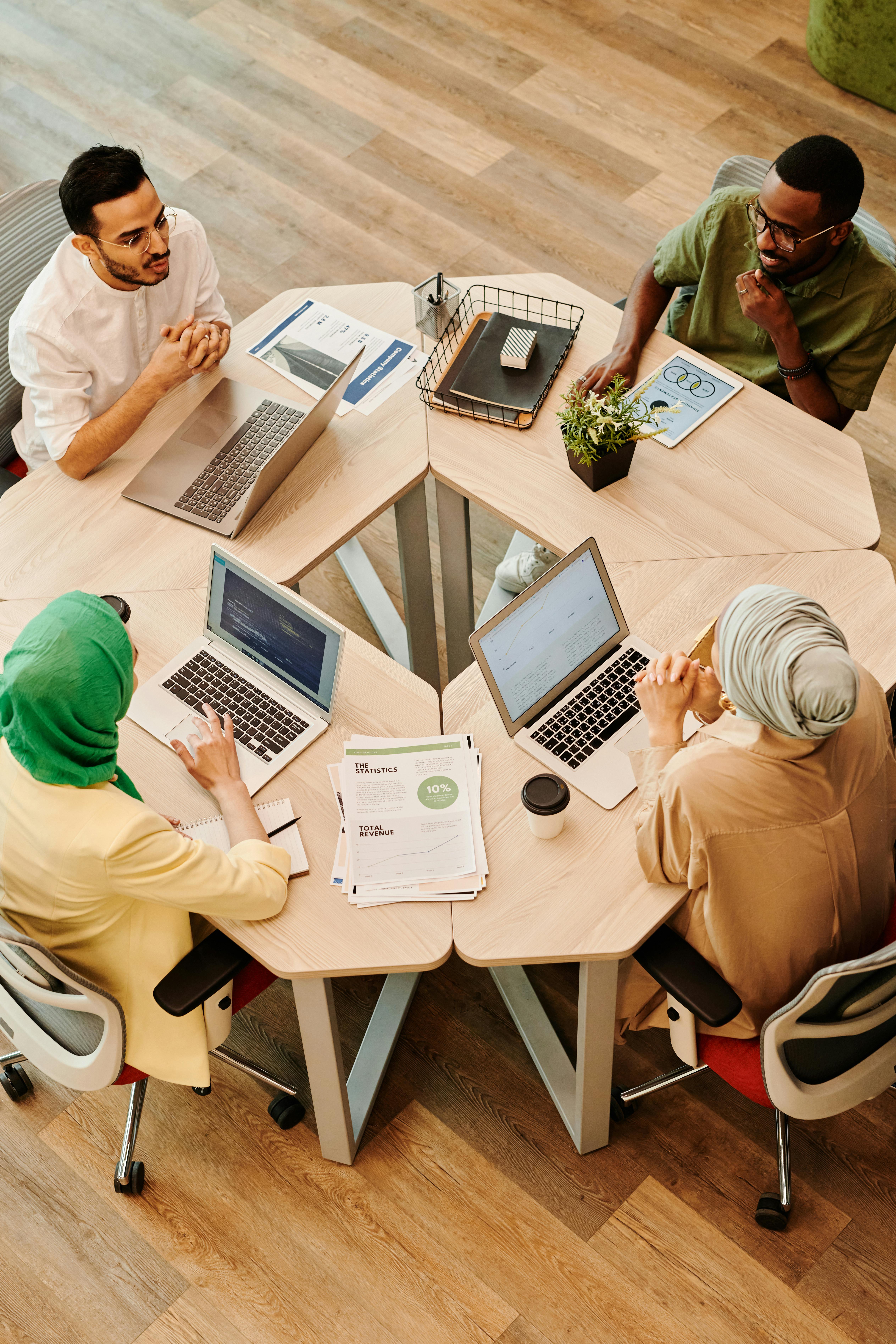 team of 4 individuals sitting around a round table with their laptops and work
